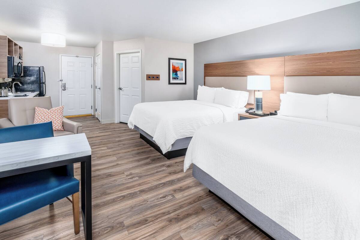 Een hotelkamer met twee bedden, een bureau, een stoel, een televisie en een deur naar de badkamer.
