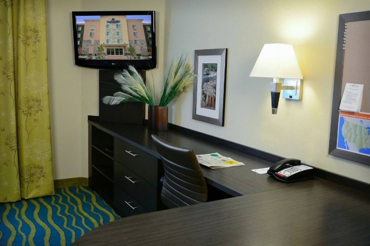 Een hotelkamer met een bureau, een telefoon, een aan de muur bevestigde televisie, een lamp en een ingelijst schilderij.