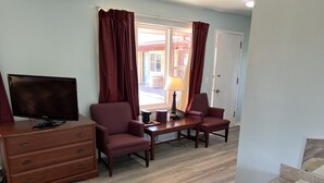 A hotel room with a wooden desk, two armchairs, a television, a lamp, and a bathtub. - Crows Nest Inn Tawas (Tawas City)