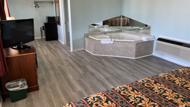 A hotel room with a large bed, a small desk with a television, a bathroom with a bathtub, and a mirror. - Crows Nest Inn Tawas (Tawas City)