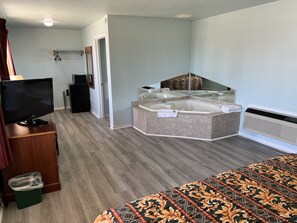 A hotel room with a large bed, a small desk with a television, a bathroom with a bathtub, and a mirror. - Crows Nest Inn Tawas (Tawas City)