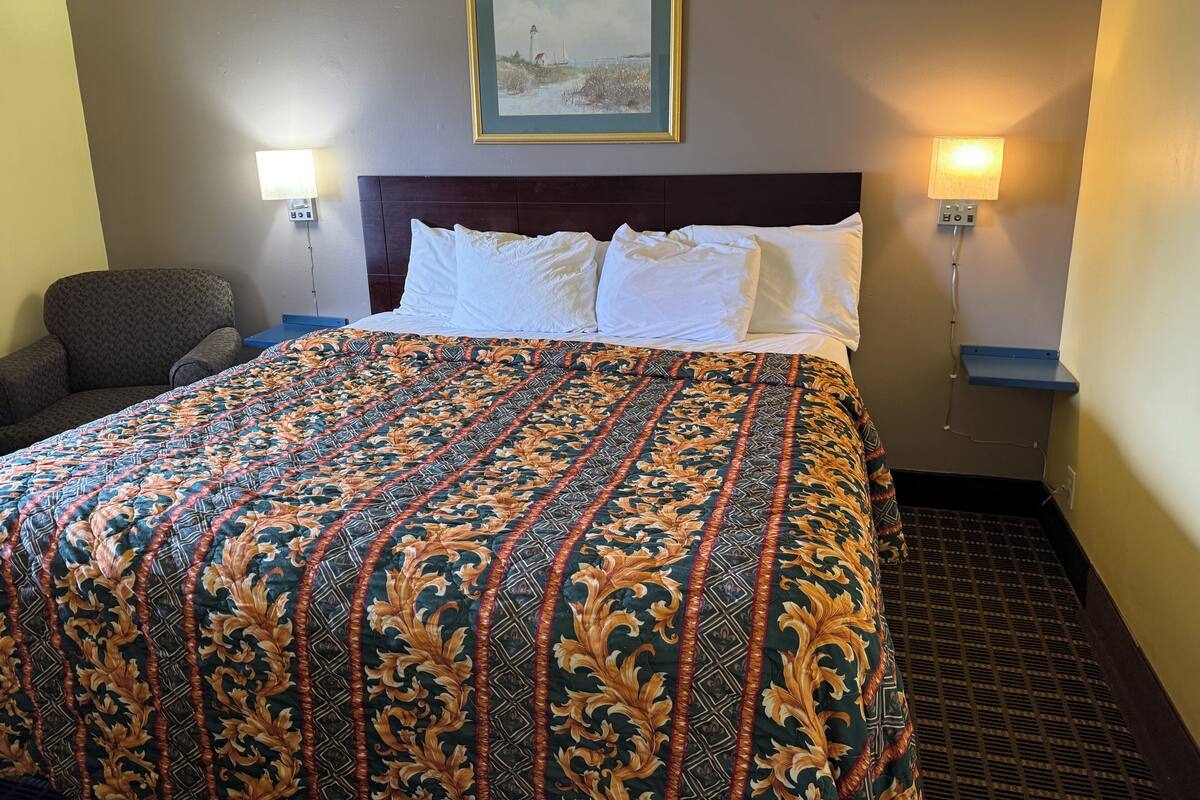 Une chambre d’hôtel avec un grand lit, deux lampes de chevet, une chaise et un tableau encadré au mur.