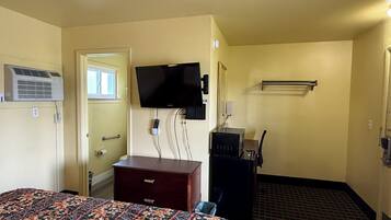 Una habitación de hotel con cama, cómoda, televisor montado en la pared, espejo y calefactor.