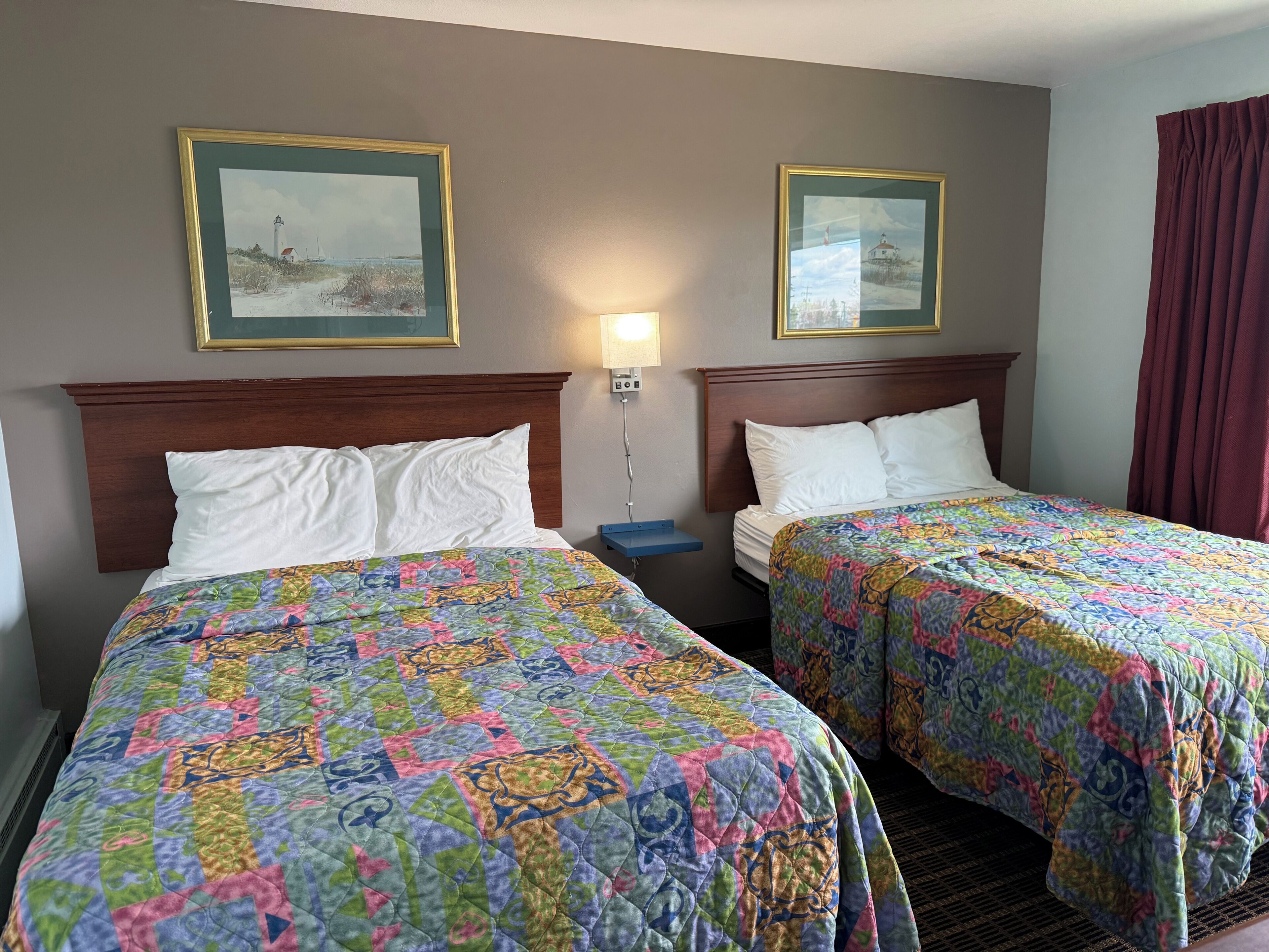 Una camera d'albergo con due letti, ognuno con una coperta colorata, un comodino, una lampada e due quadri appesi al muro.