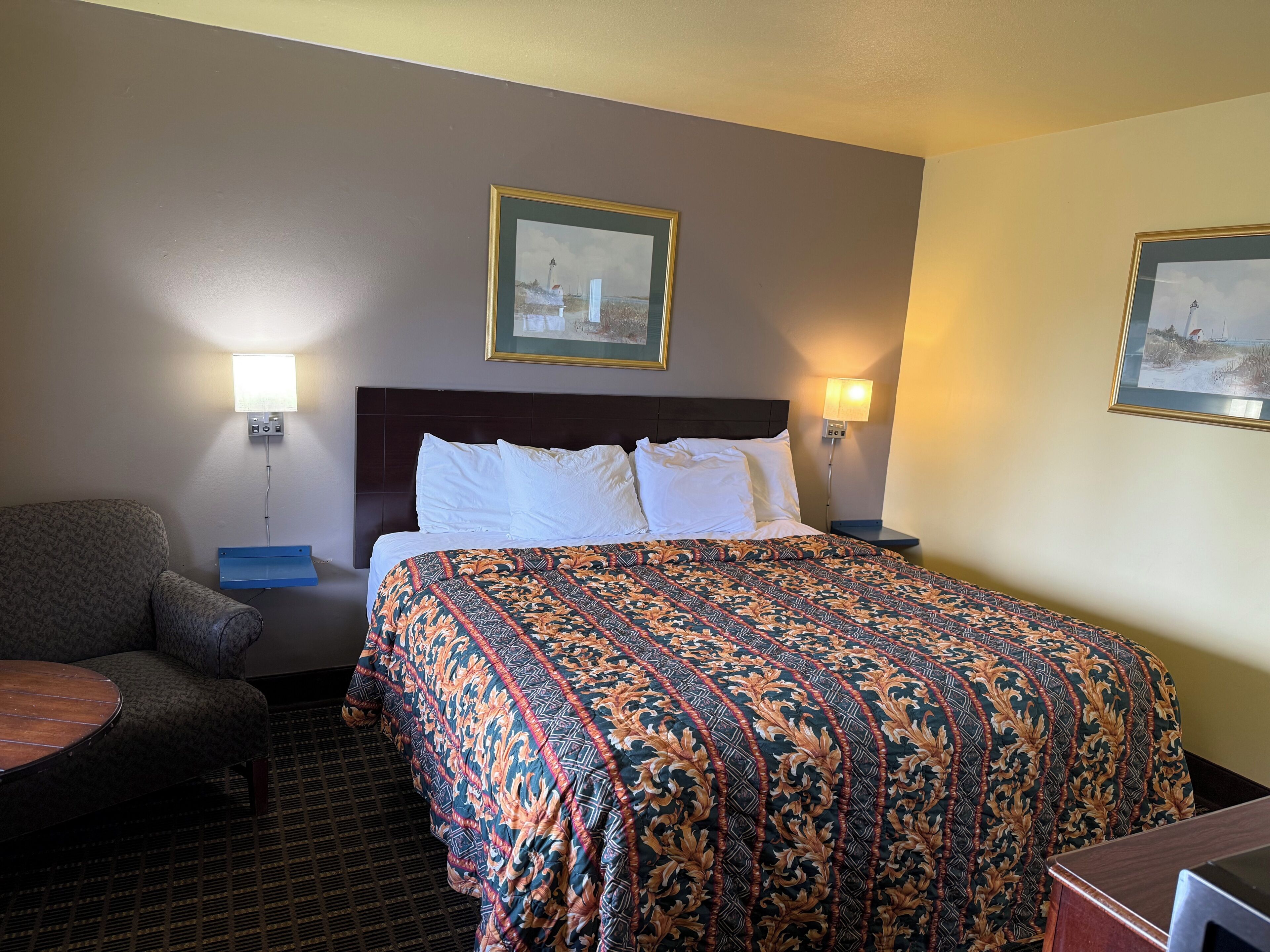 A hotel room with a bed, two bedside lamps, a chair, and two framed pictures on the wall.