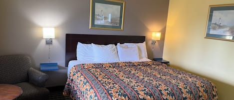 Una habitación de hotel con una cama, dos lámparas de noche, una silla y dos cuadros en la pared.