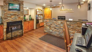 Eine moderne Lobby mit Kamin aus Stein, Holzelementen, einer Rezeption und einem Wandfernseher.