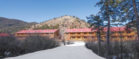 A lodge with a red roof, situated in a snowy landscape with a mountain in the background.
