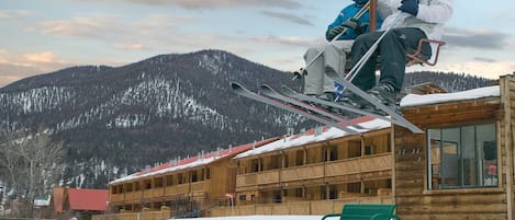 Un edificio de madera con un telesilla, suelo cubierto de nieve y una montaña al fondo.