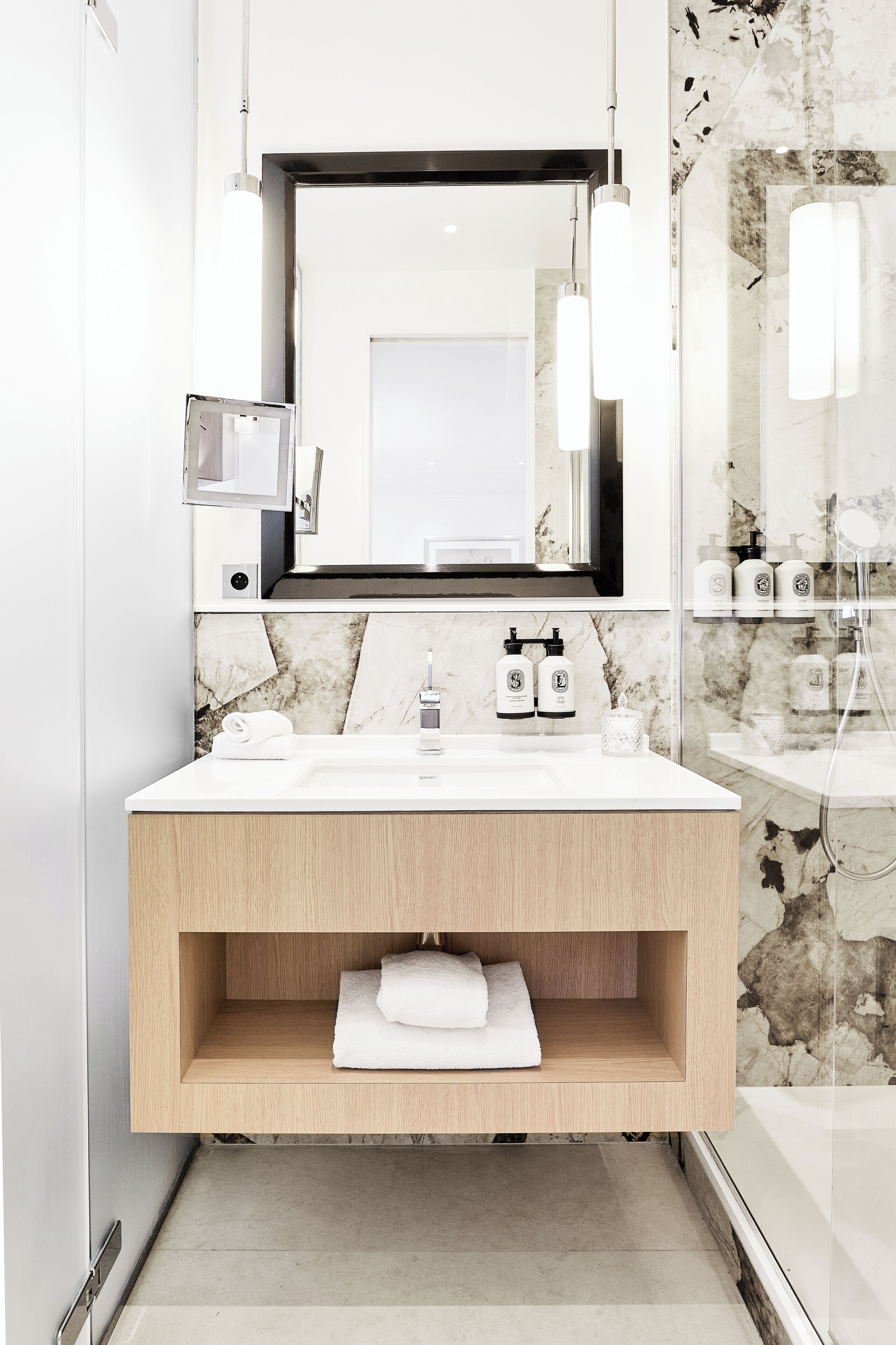 Un baño moderno con un revestimiento de mármol, un mueble de tocador de madera, un espejo grande y una cabina de ducha de vidrio.