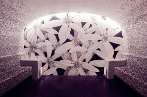 A room with a large, floral-patterned headboard, two patterned armchairs, and a dark floor.