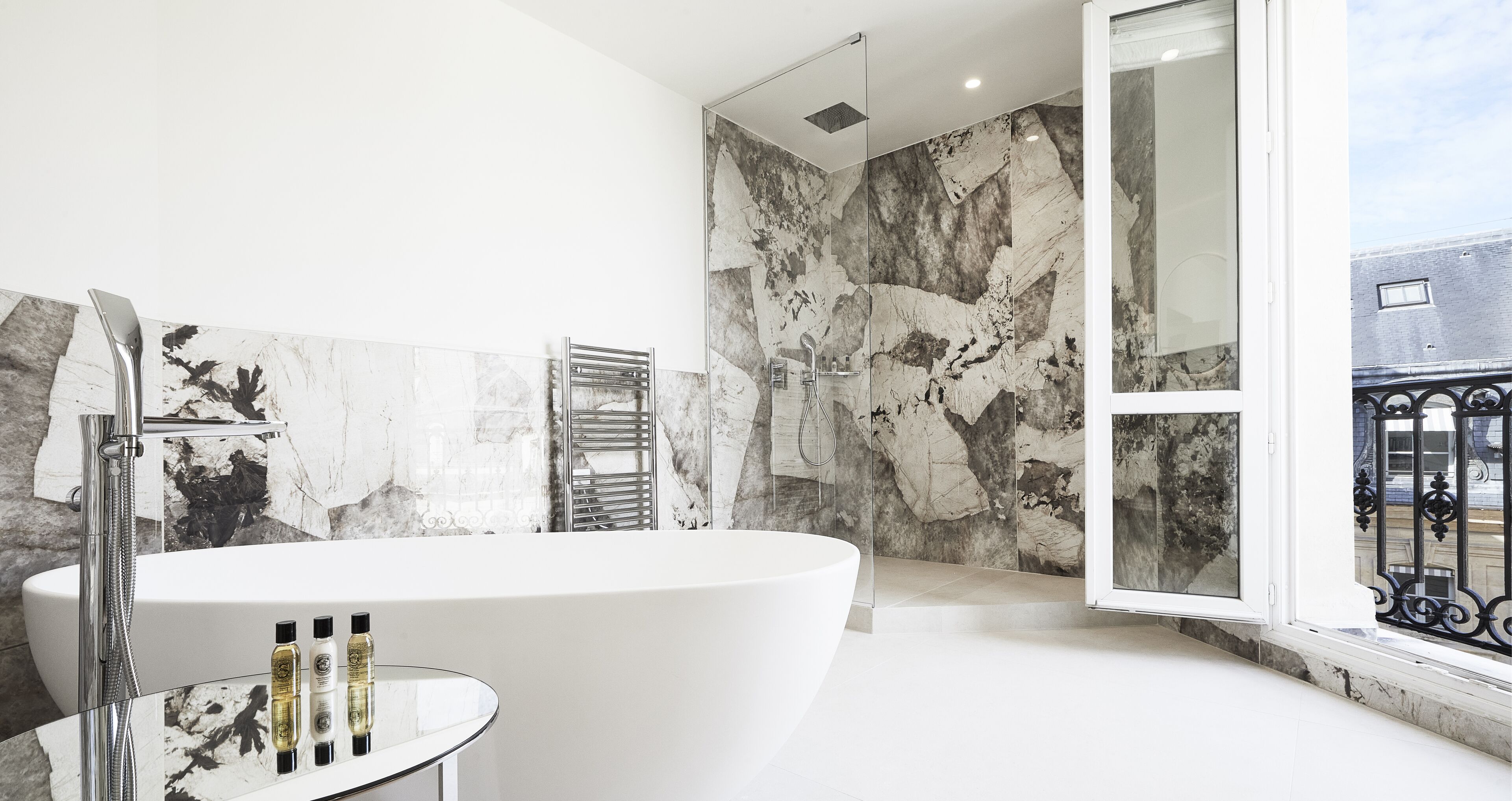 A modern bathroom with a freestanding bathtub, a glass shower enclosure, and a large window with a view of the city.