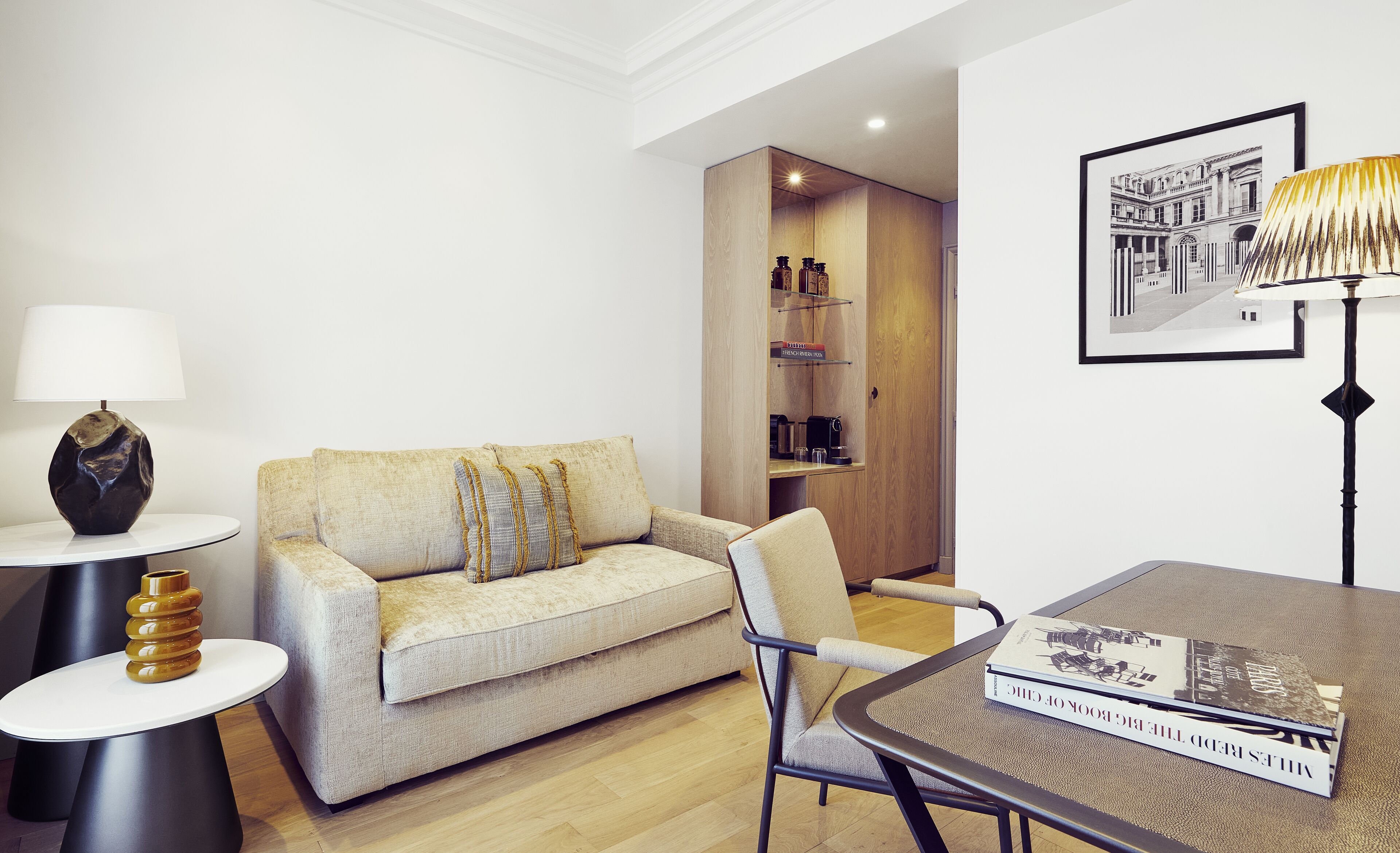 A modern living room with a sofa, a side table, a chair, and a coffee table. There is a bookshelf with books and a framed picture on the wall.