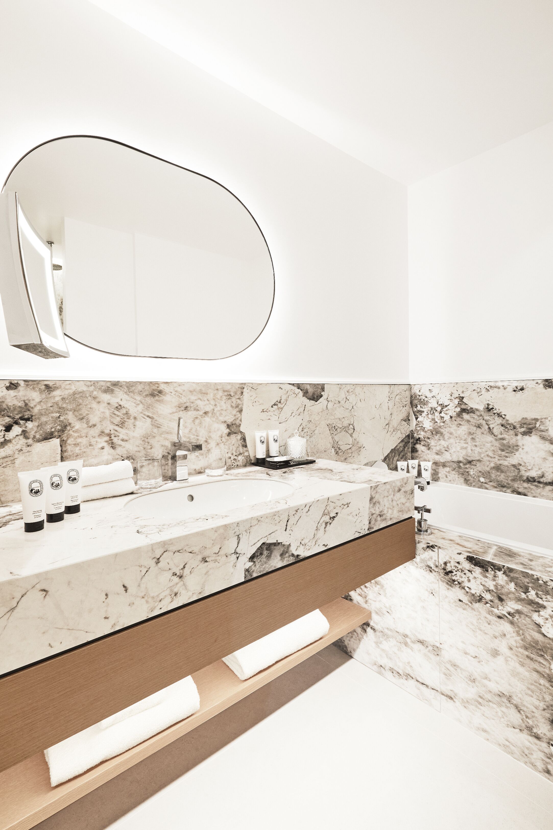 A modern bathroom with a marble sink, a large mirror, and a bathtub.