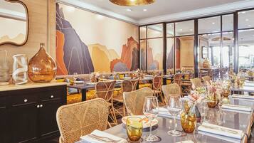 Un restaurante con una larga mesa dispuesta para varios comensales, sillas de mimbre y un mural grande en la pared.
