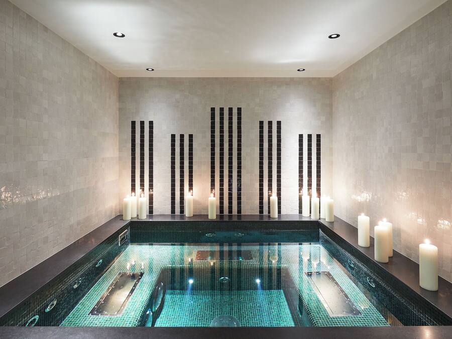 A modern spa room with a rectangular hot tub, tiled walls, and candles.
