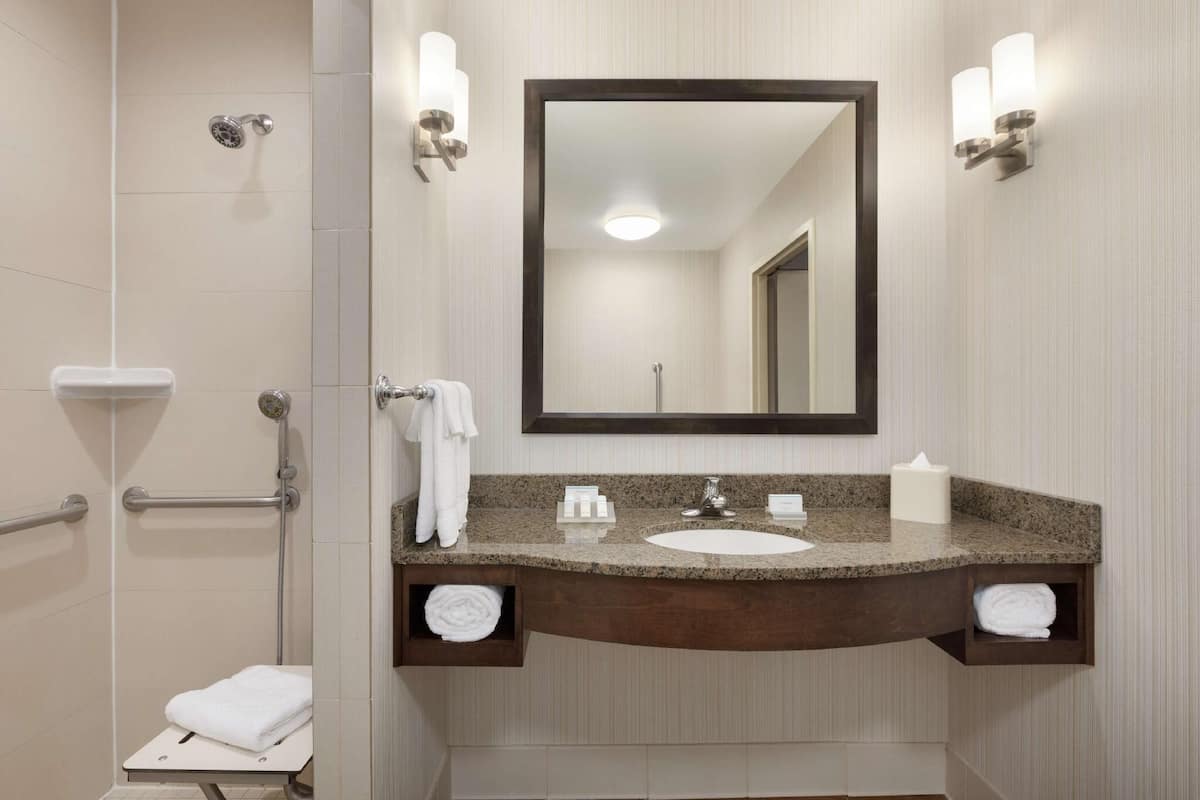 A bathroom with a shower, a sink with a mirror, and a towel rack.