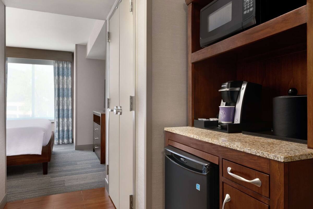 A hotel room with a bed, a kitchenette with a coffee maker, a microwave, and a refrigerator.