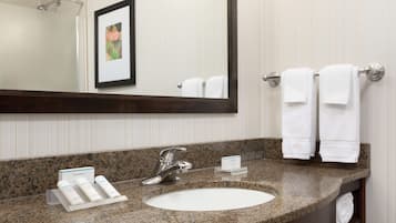 A bathroom with a granite countertop, a white sink, a framed picture on the wall, and a towel rack with two white towels.