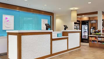 Zona de recepción de hotel con una pared azul, un mostrador con el letrero 'Hilton', un refrigerador y una máquina expendedora.