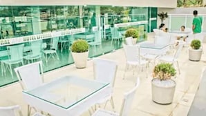 An outdoor patio area with glass tables and white chairs, surrounded by potted plants. - Hotel Litoral Fortaleza (Fortaleza)