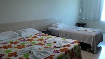 Ein Hotelzimmer mit zwei Betten, jeweils mit floralem Überwurf und weißen Laken. Im Raum befindet sich ein kleiner Tisch und eine Bank.