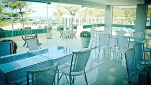 An outdoor seating area with glass tables and chairs, a view of the surrounding area, and a sign indicating a restaurant. - Hotel Litoral Fortaleza (Fortaleza)