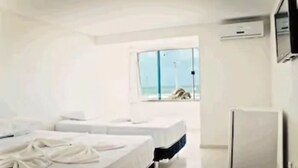 A hotel room with two beds, a small table, and a window with a view of the beach. - Hotel Litoral Fortaleza (Fortaleza)
