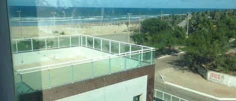 A view from a balcony with a glass railing overlooking a beach and a parking area.