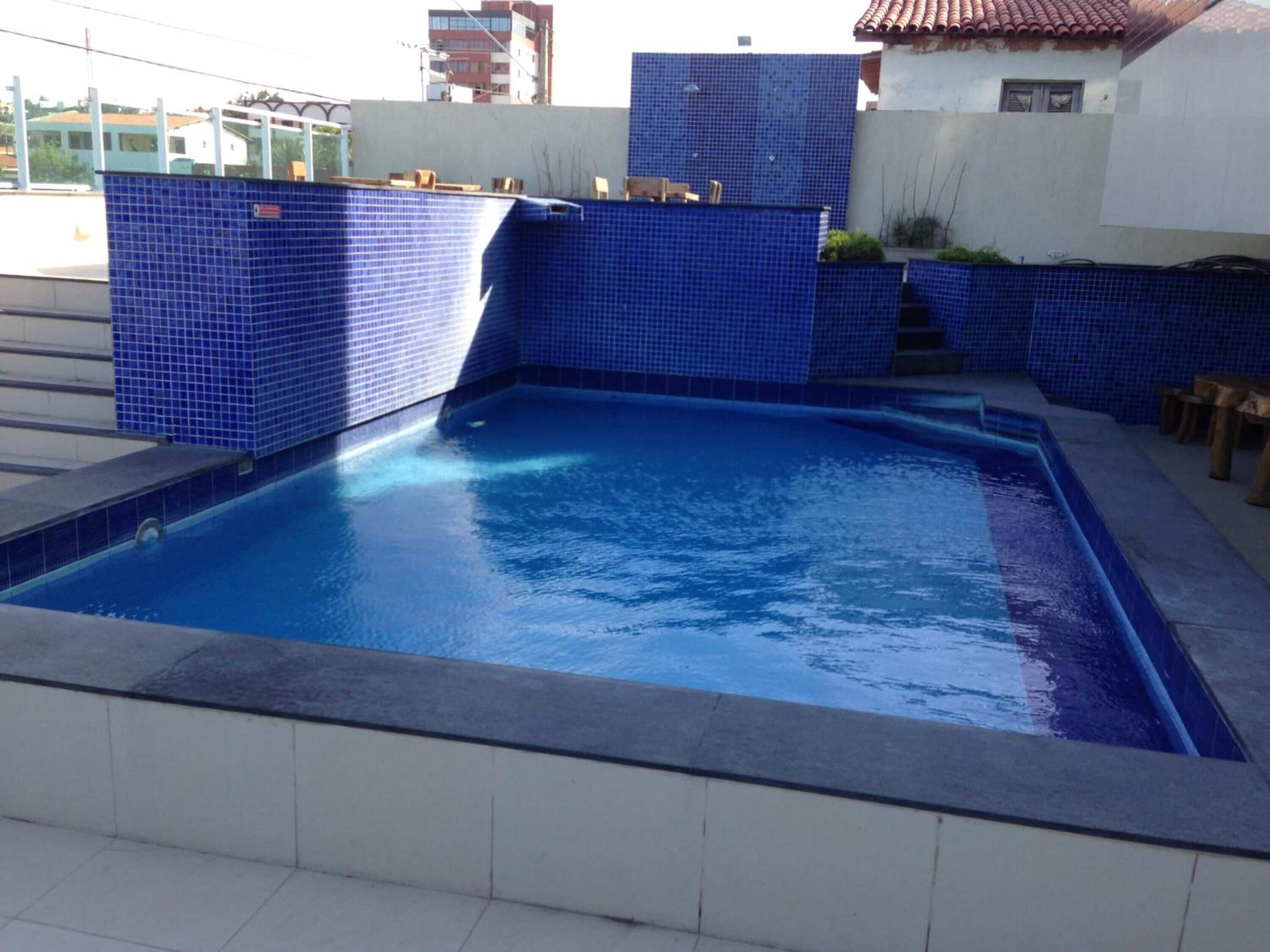 A rectangular swimming pool with blue tiles, surrounded by a white tiled deck.