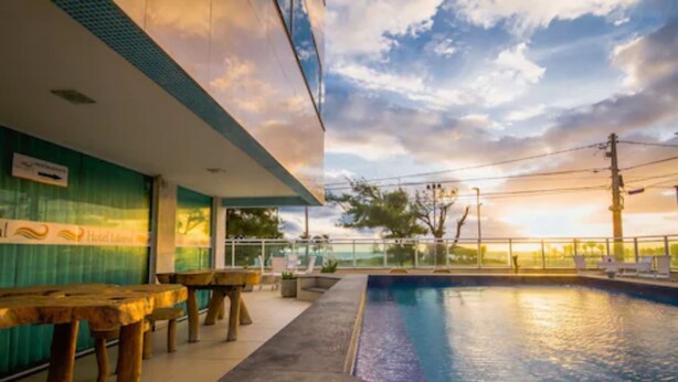 A pool area with a sunset view, wooden tables, and a sign indicating a hotel lobby. - Hotel Litoral Fortaleza (Fortaleza)