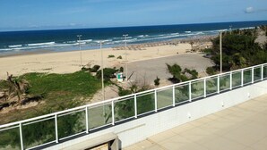 A beach with a clear view of the ocean, a sandy area with some vegetation, and a white railing in the foreground. - Hotel Litoral Fortaleza (Fortaleza)