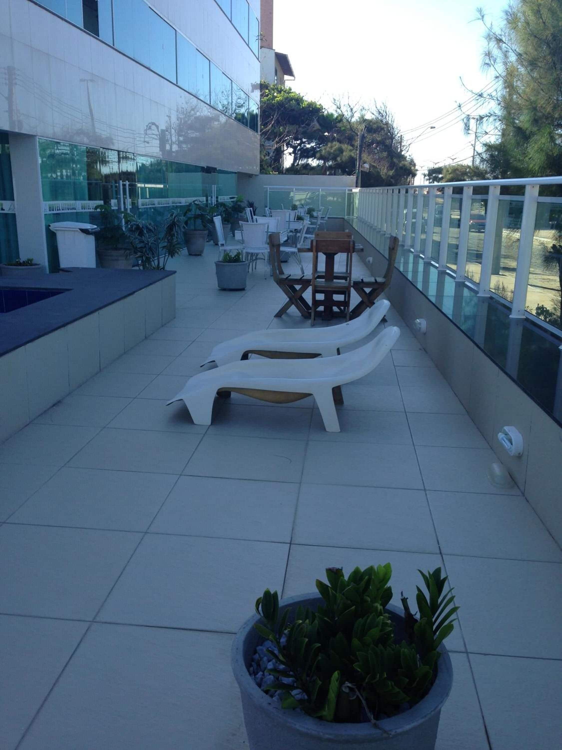 An outdoor terrace with white lounge chairs, potted plants, and a glass railing.