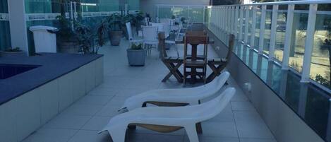 An outdoor terrace with white lounge chairs, potted plants, and a glass railing.