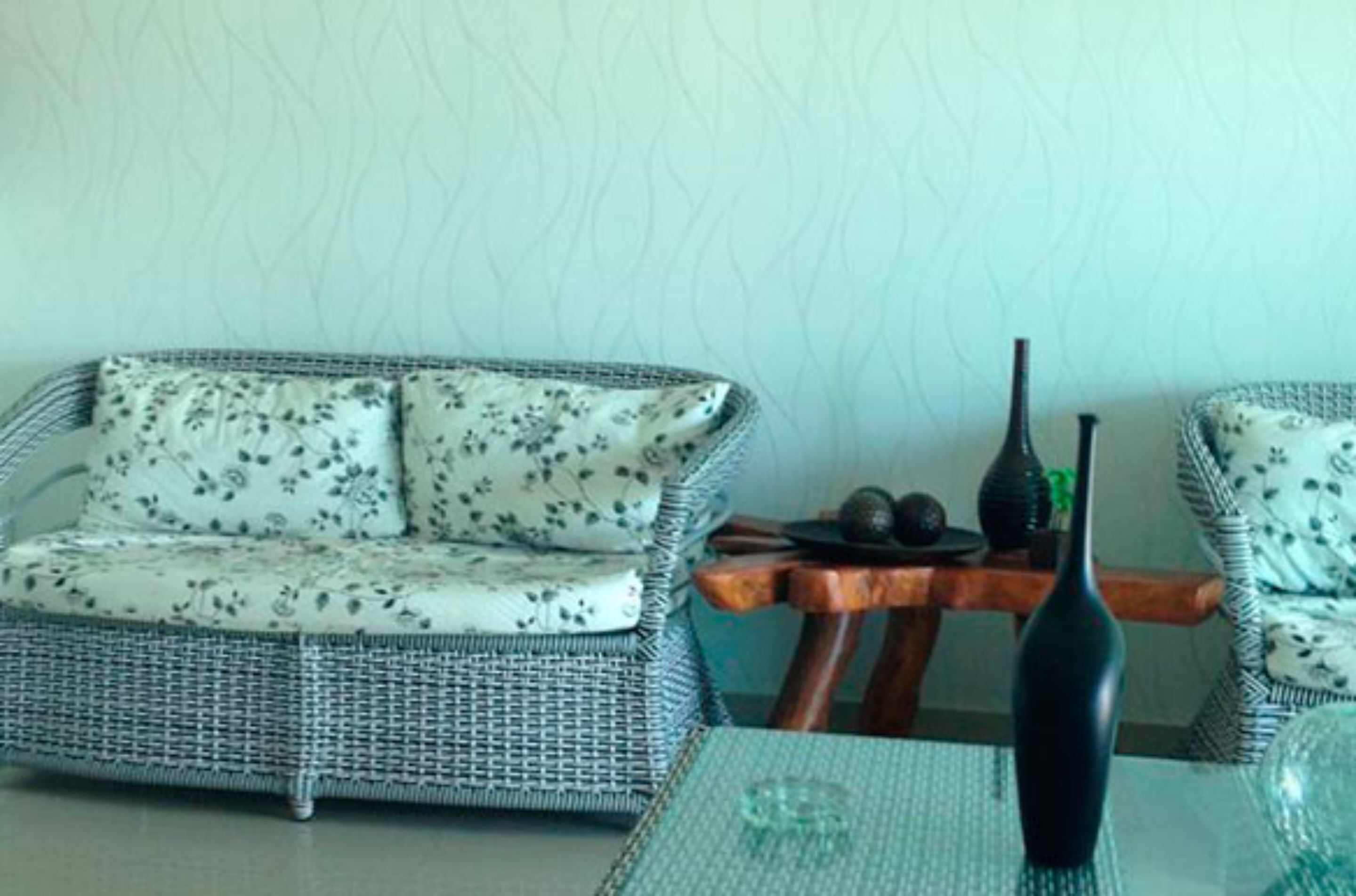 A wicker sofa with floral cushions, a small wooden table with a vase, and a textured wall.