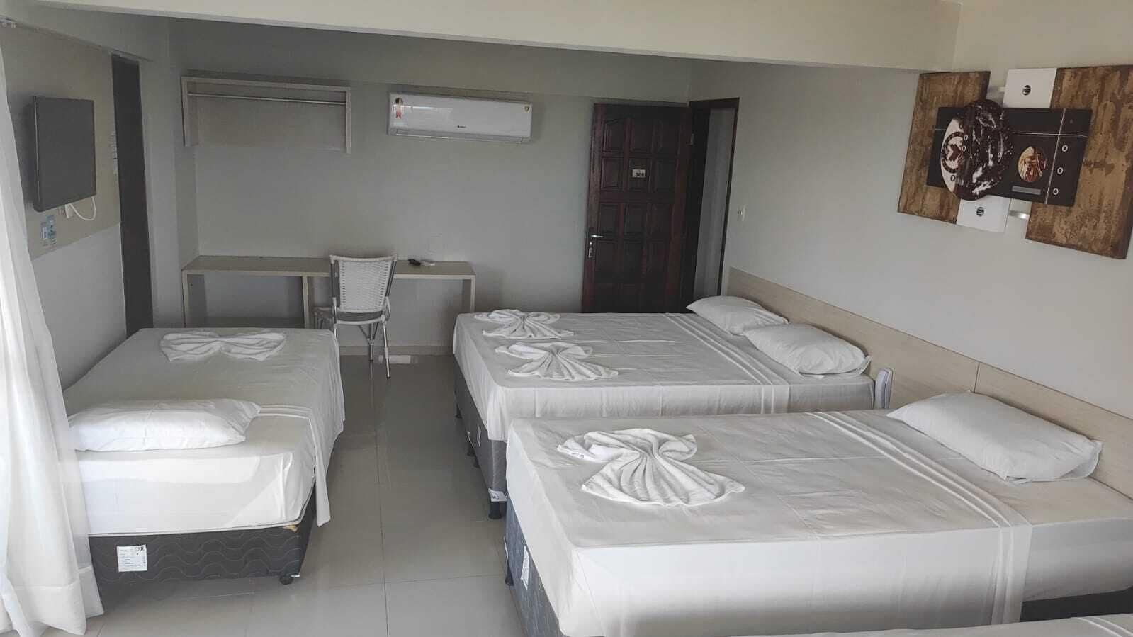 Habitación de hotel con tres camas, un escritorio, una silla y una puerta.