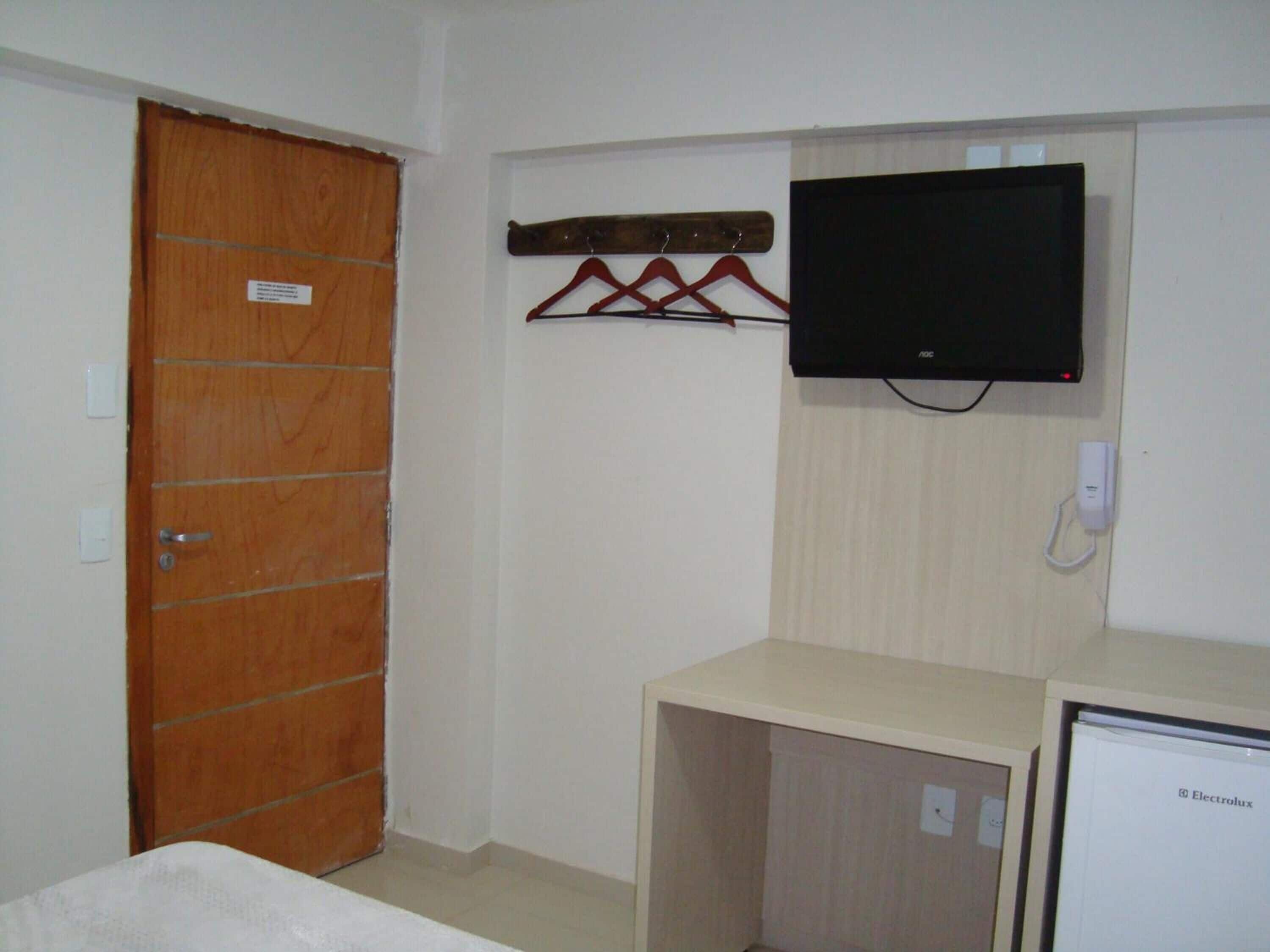A room with a wooden door, a mounted television, and a small cabinet.