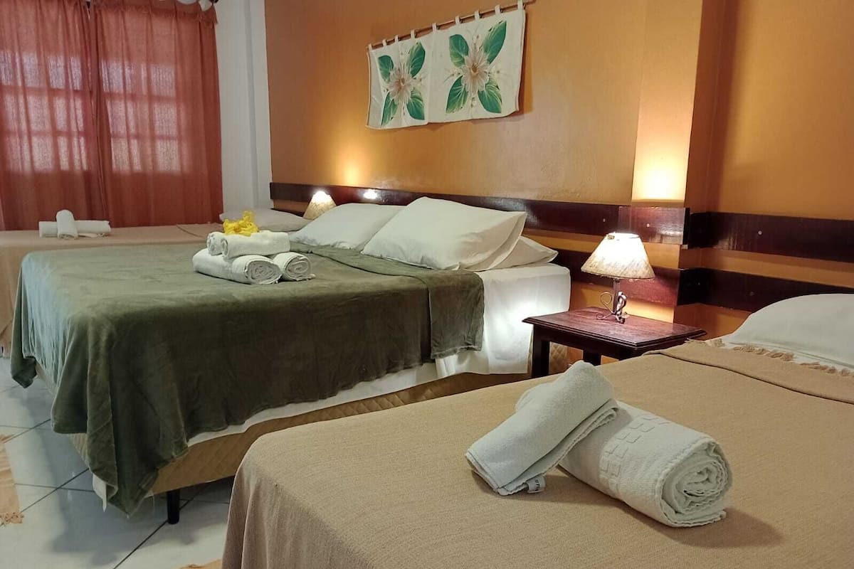 Ein Hotelzimmer mit zwei Betten, jeweils mit einer grünen Tagesdecke und weißen Kissen, einem Nachttisch mit Lampe und einer Wand mit einem floralen Gemälde.