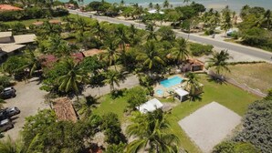 An aerial view of a coastal property with a swimming pool, palm trees, and a beach in the background. - Pousada Aldeia Portuguesa (Santa Cruz Cabralia)
