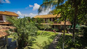 A courtyard with a paved path, palm trees, and a building with a tiled roof. - Pousada Aldeia Portuguesa (Santa Cruz Cabralia)