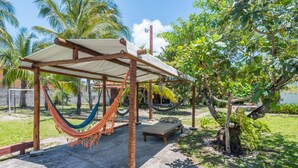 A hammock under a wooden pergola in a garden with palm trees and a bed. - Pousada Aldeia Portuguesa (Santa Cruz Cabralia)