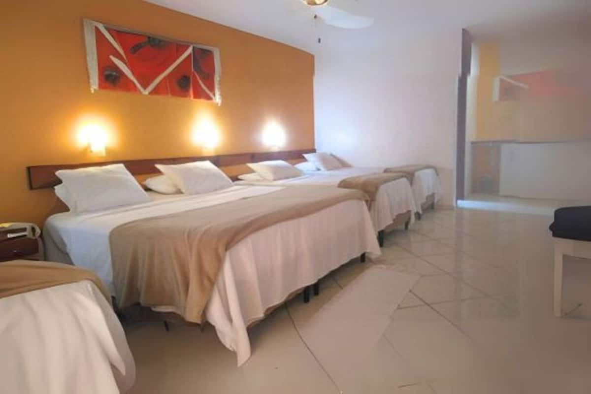 Ein Hotelzimmer mit drei nebeneinander stehenden Betten, einem großen Fenster und einem Deckenventilator.