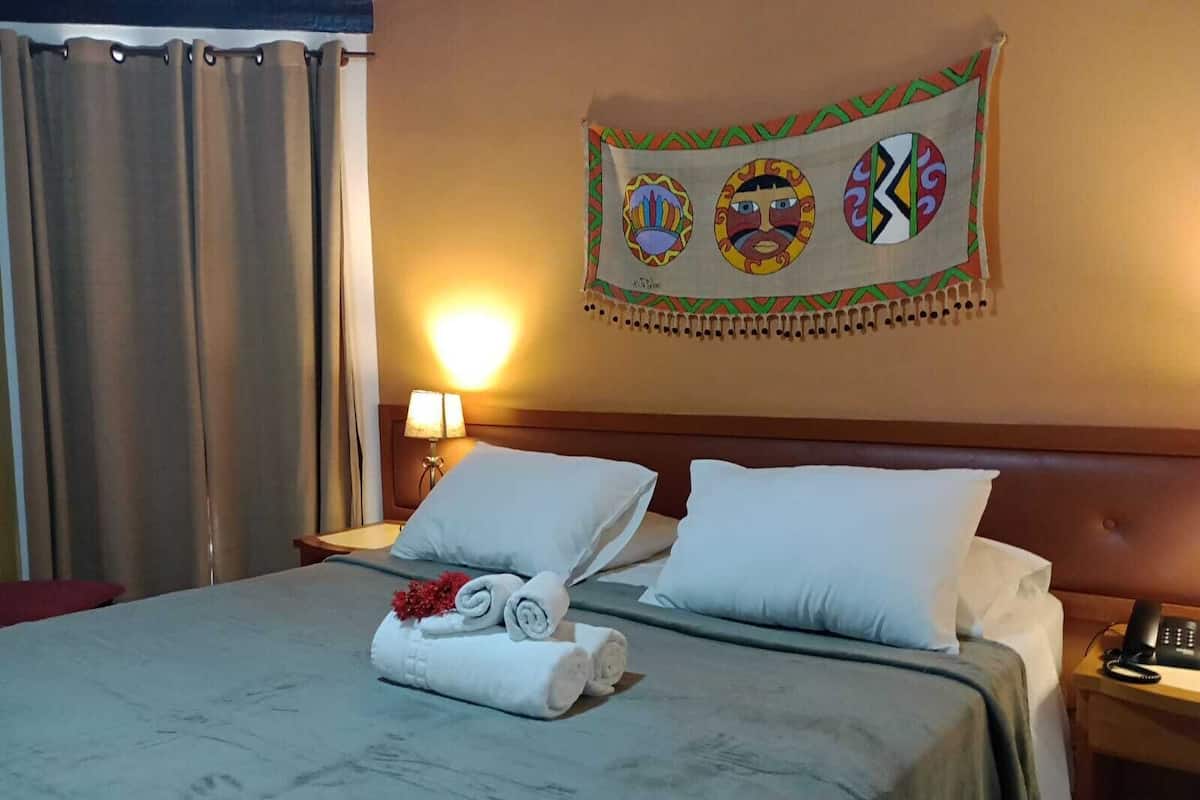 Ein Hotelzimmer mit Bett, zwei Kissen, einem Nachttisch mit Lampe und Wandteppich.