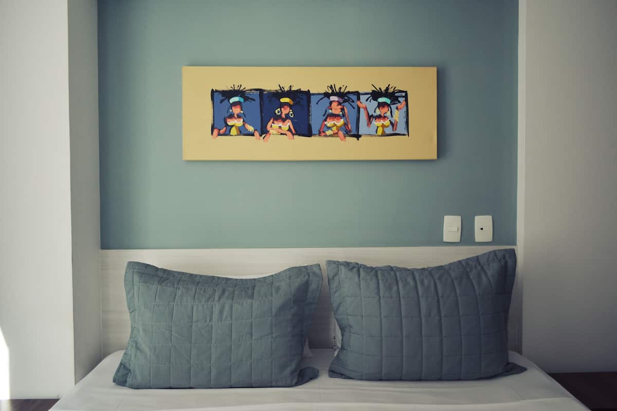 A bedroom with a bed, two pillows, and a wall-mounted painting.