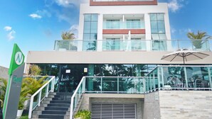 A modern hotel with a glass facade, a staircase leading to the entrance, and outdoor seating with umbrellas. - Nord Easy Ondas do Atlântico (João Pessoa)
