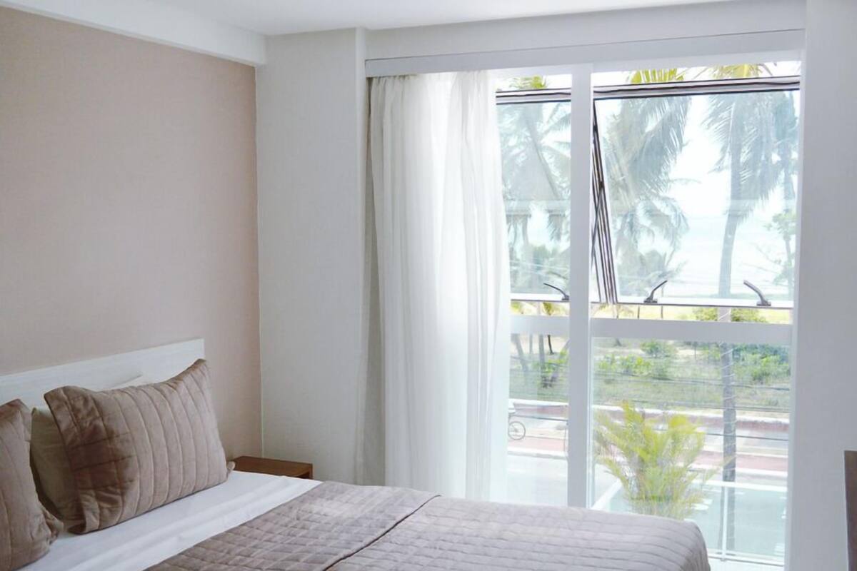A bedroom with a large bed, a window with curtains, and a view of palm trees.
