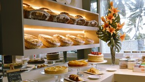 A buffet with various baked goods and desserts displayed on shelves and counters. - Nord Easy Ondas do Atlântico (João Pessoa)