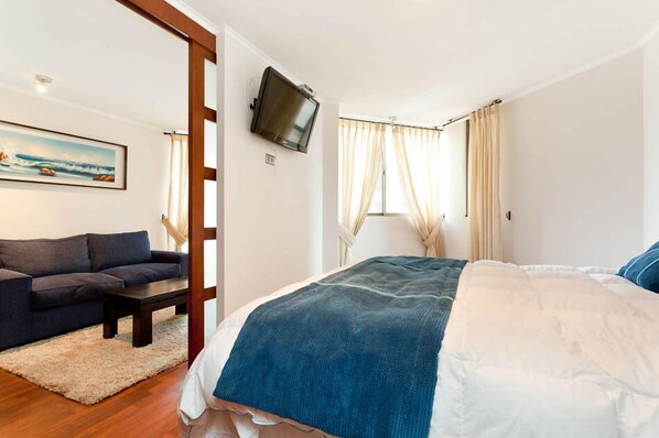 A bedroom with a bed, a sofa, a television, and a painting on the wall.