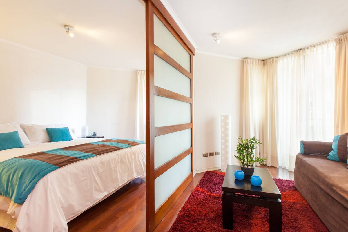 A hotel room with a bed, a sofa, a coffee table, and a window with curtains.