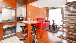 A modern kitchen with a gas stove, a dining area with a wooden table and bar stools, a red sofa, and a staircase. - ECO PLAZA Santiago (Santiago)